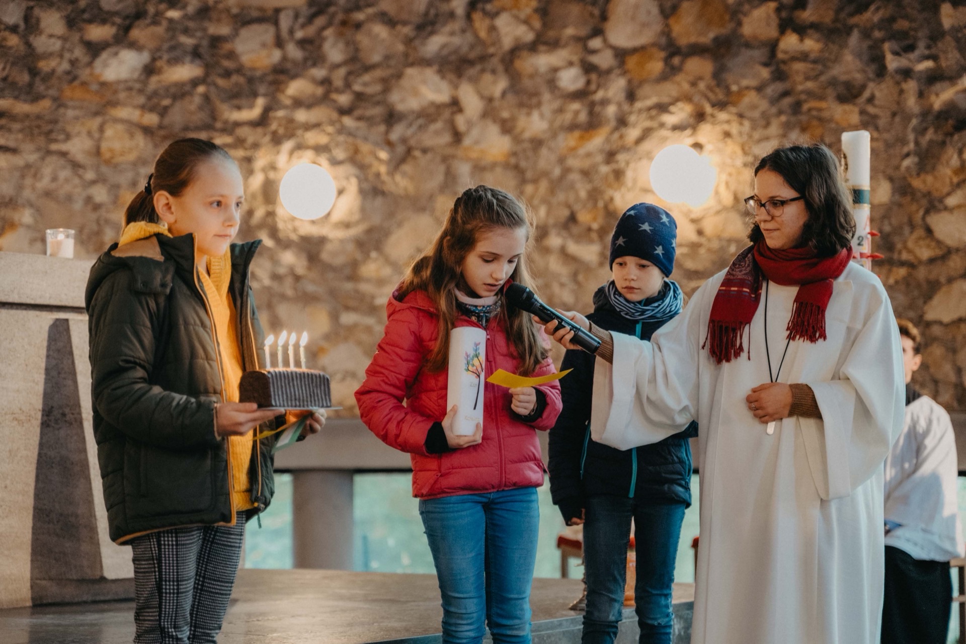 Kinder bei kirchlicher Feier mit Kerzen und Mikrofon