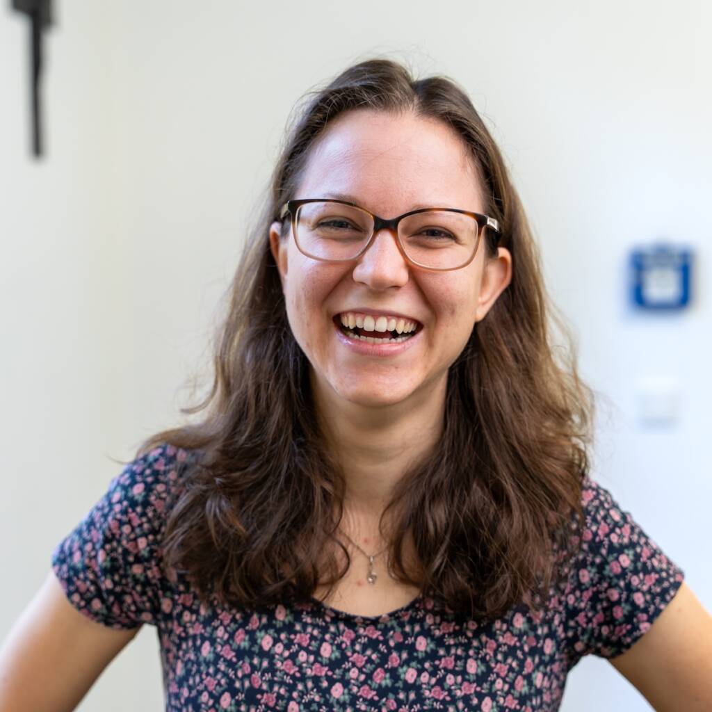 Lachende Frau mit Brille vor weißem Hintergrund.