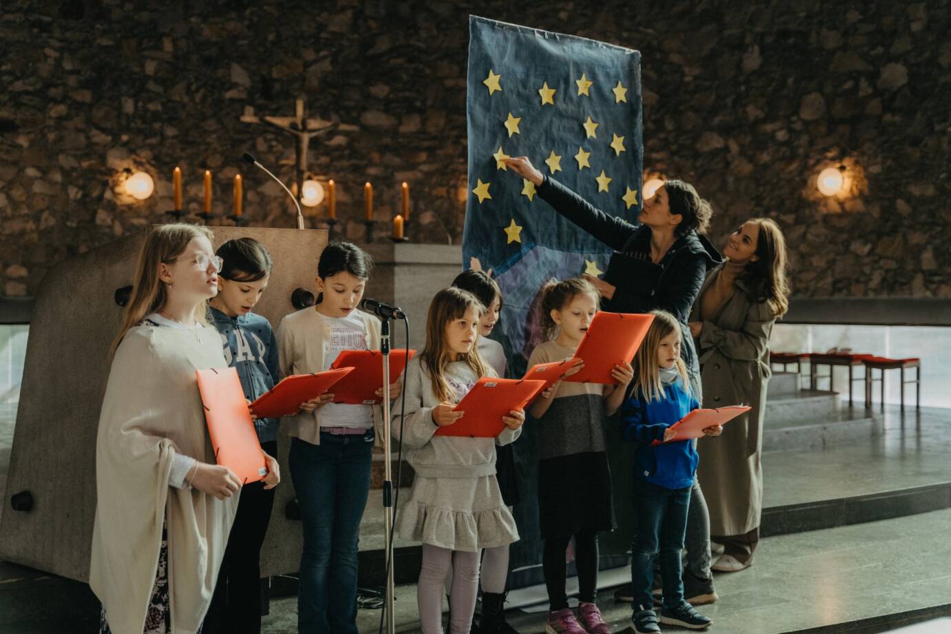 Kinder singen in einer Kirche vor einem Poster.
