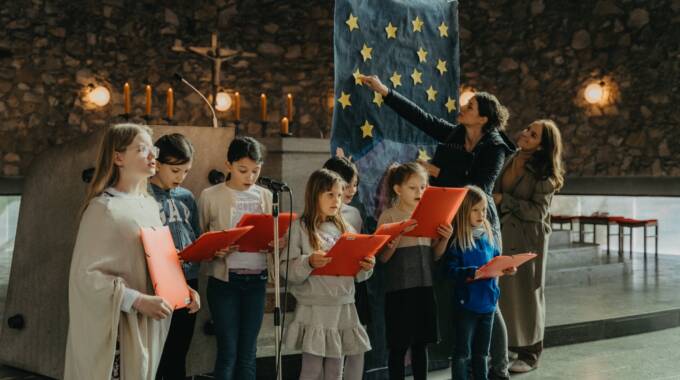 Kinder singen in einer Kirche vor einem Poster.