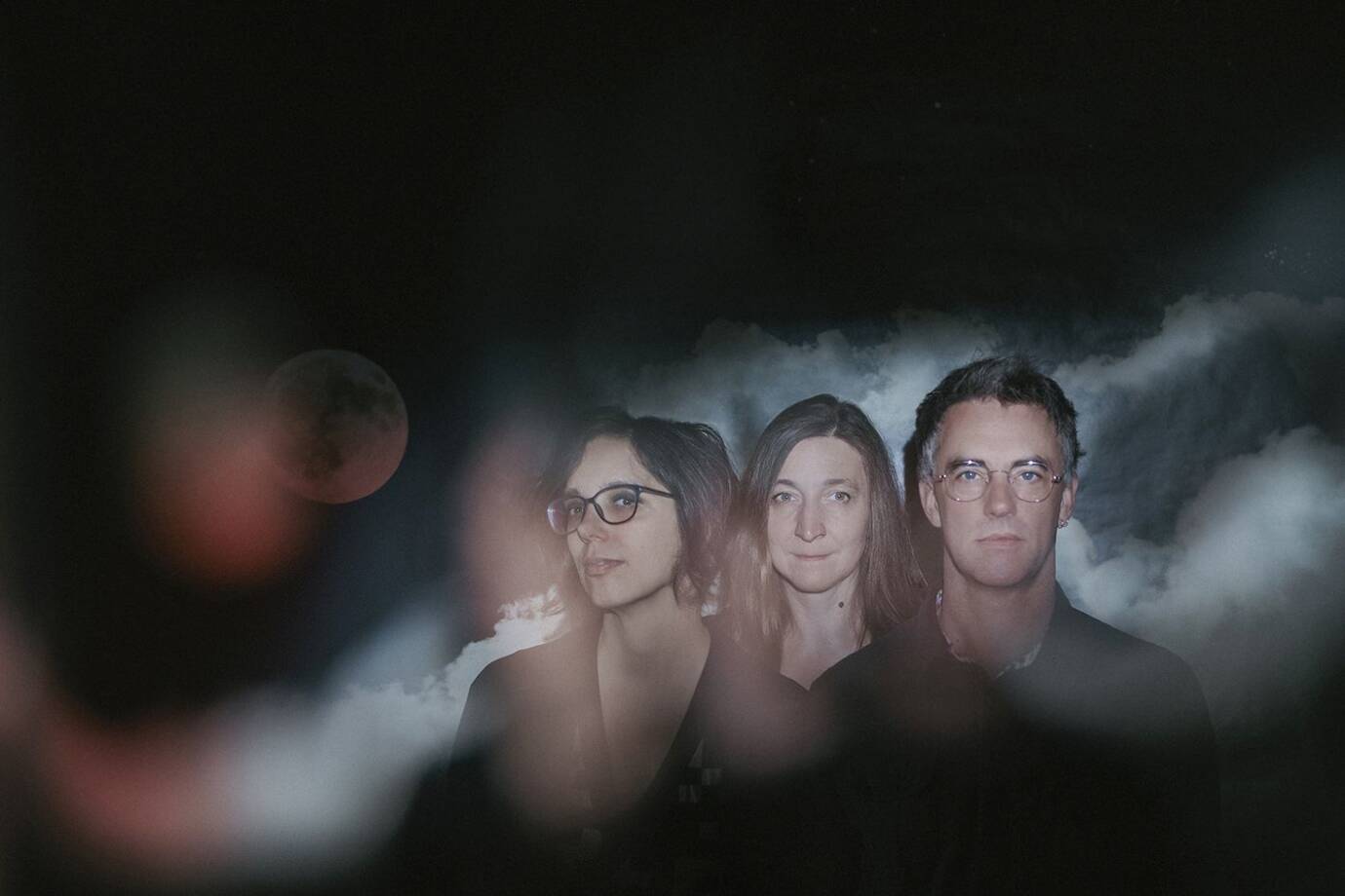 Drei Personen vor wolkigem Hintergrund mit Mond