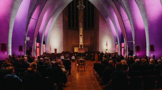 Kircheninnenraum mit lila Licht und Gottesdienstbesuchern