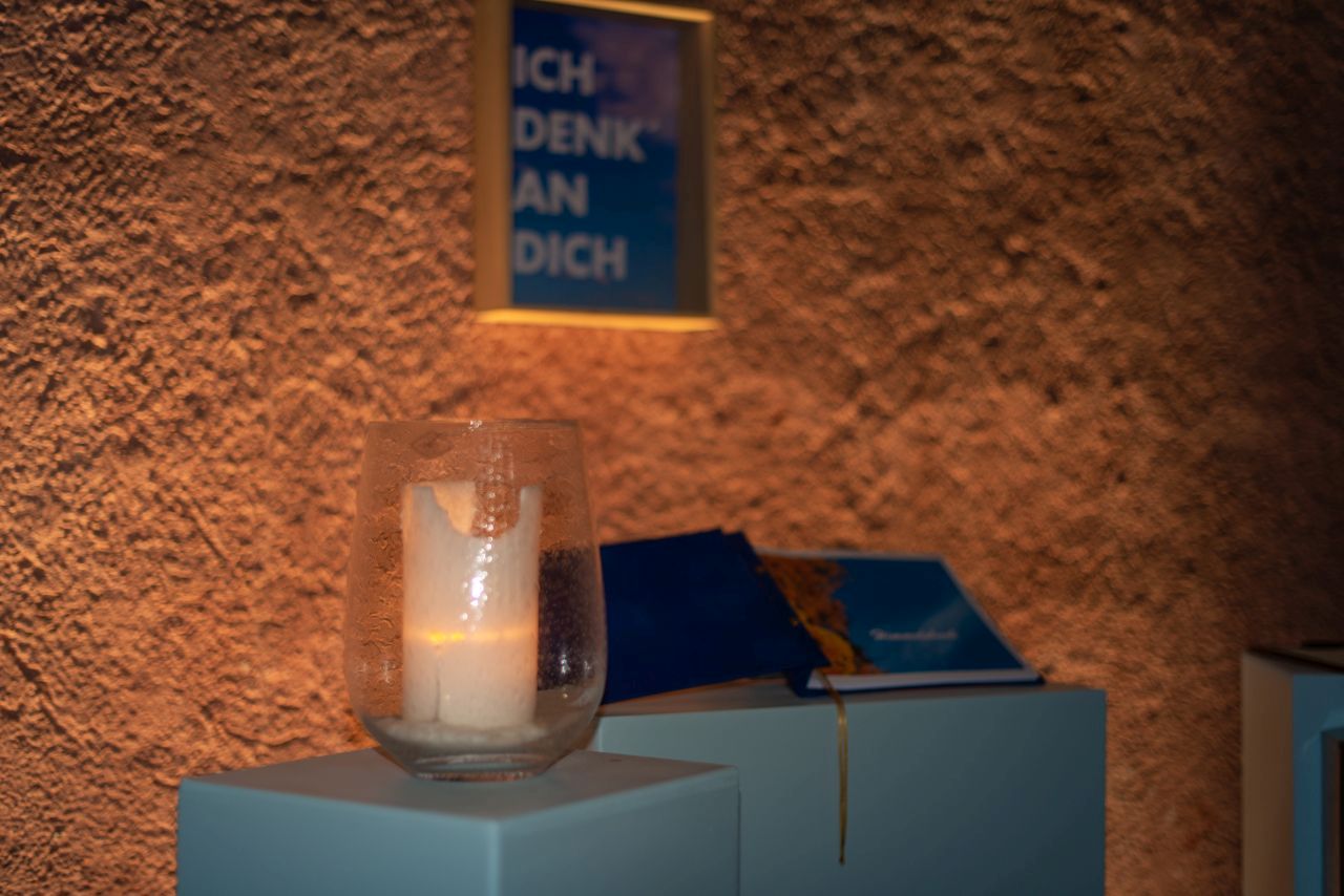 Brennende Kerze neben blauem Buch auf Podest