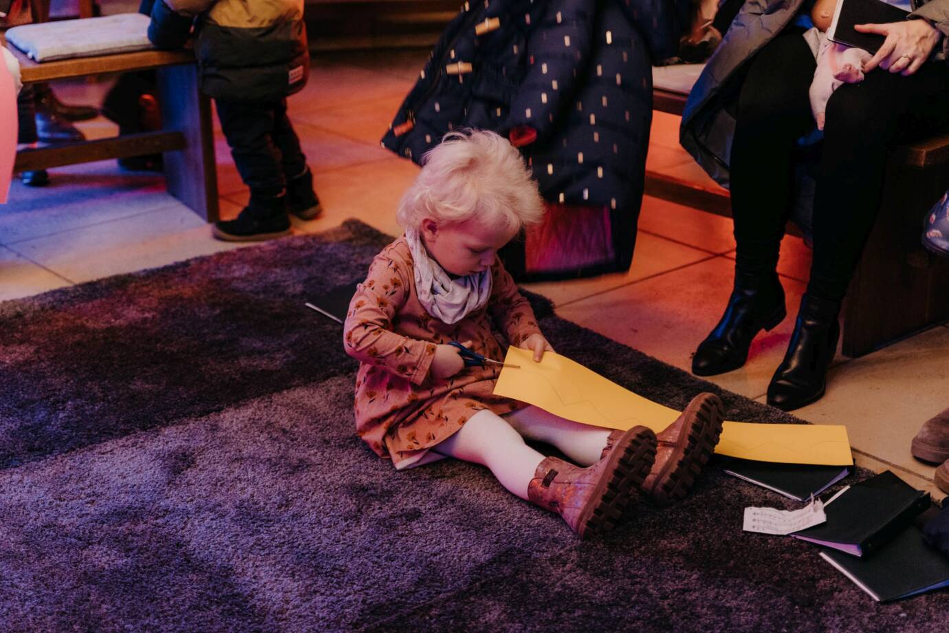 Kind schneidet gelbes Papier auf Teppichboden