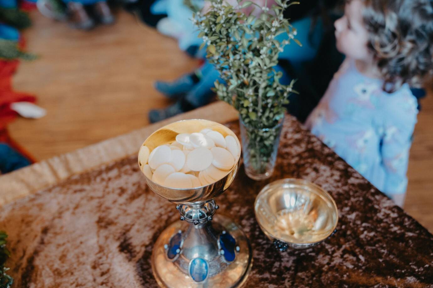 Kind betrachtet Kelch mit Hostien und Zweig