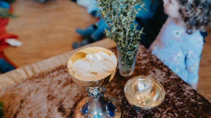 Kind betrachtet Kelch mit Hostien und Zweig