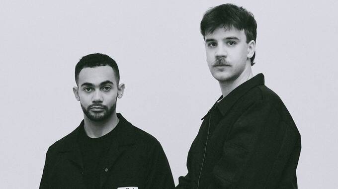 Zwei Männer in schwarzen Jacken vor grauem Hintergrund