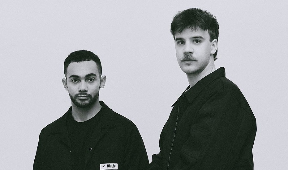 Zwei Männer in schwarzen Jacken vor grauem Hintergrund