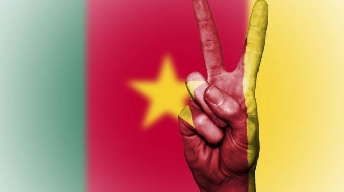 Hand zeigt Friedenszeichen vor Kamerun-Flagge