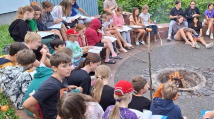Kinder sitzen mit Büchern am Lagerfeuer