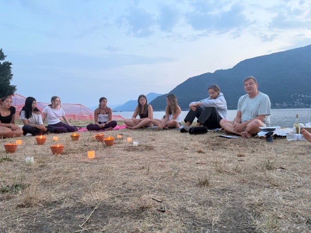 Menschen sitzen im Kreis mit Kerzen am See