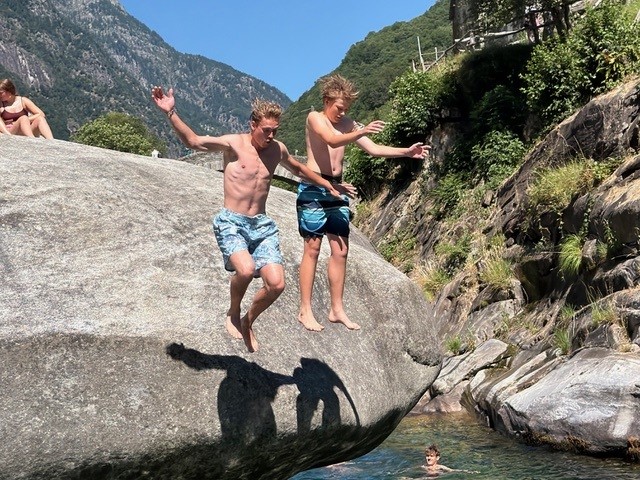 Zwei Jungen springen von Felsen ins Bergwasser